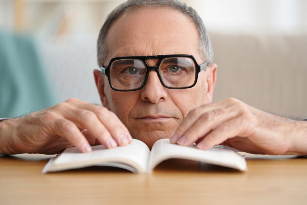 Büyüteçli okuma gözlüğüyle kitap okuyan adam — Beş Optik İzmir