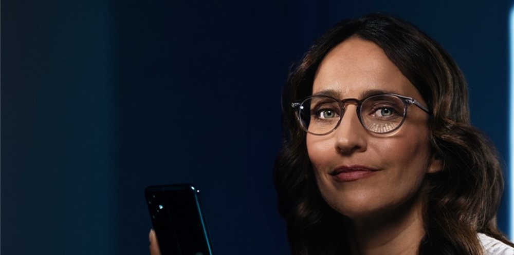 Loş ışıkta elinde telefon tutan gözlüklü kadın
