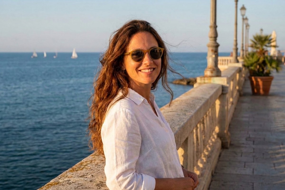 Gün batımında deniz kenarındaki bir kordonda korkuluğa yaslanmış, Serengeti Raffaele bal rengi yuvarlak güneş gözlüğü takan gülümseyen kadın